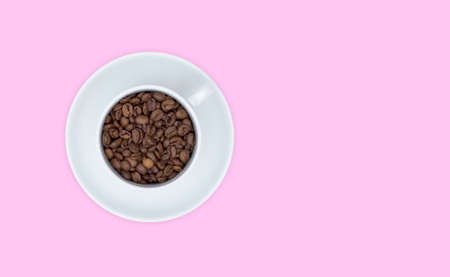 White Cup and saucer, full Cup of coffee beans. Top view, pink background. Free space for text.の写真素材