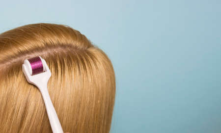 Hand and mesoroller in hand on a blue background. Scalp and skin care, healthy hair.の写真素材