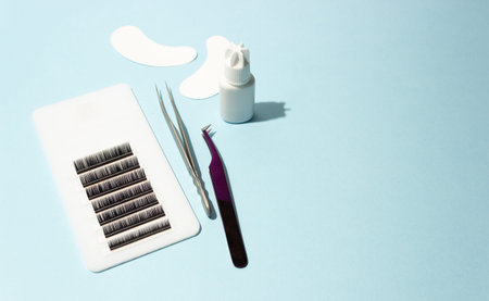 Artificial eyelashes on a white tablet, glue, patches and tweezers with shadow on a blue background....