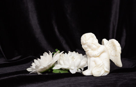 Little angel with wings on a black background and flowers, free space for text. Concept of memory of...