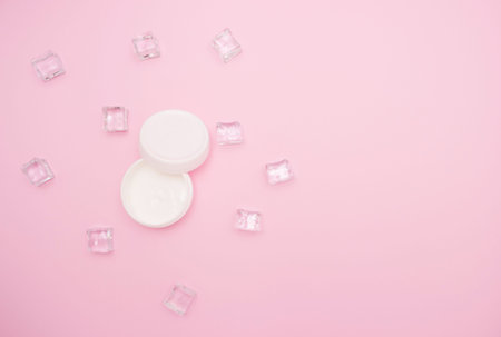 Body and skin care, cosmetology. Open white jar of cream, ice cubes. Top view, pink background, free space for text.の写真素材