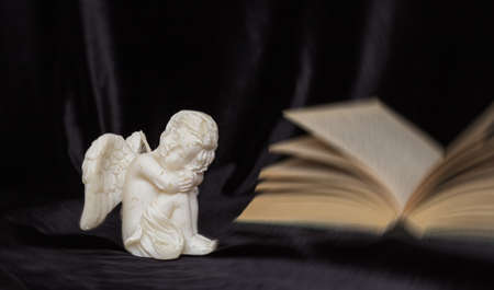 A small angel with wings on a black background and a book, free space for text. Concept of memory of a person, funeral.の写真素材