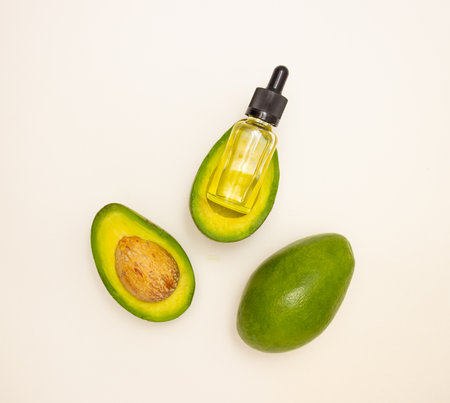 Glass bottle with pipette and avocado oil and avocado fruit on a light background, top view. Face and body skin care and healthy nutrition.の写真素材