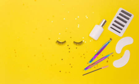 Eyelash extension tools and artificial eyelashes on a yellow background. The view from the top.