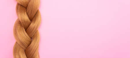 Braid of light brown artificial hair on a pink background, free space for text. The concept of a hair salon, hair extensions.の写真素材
