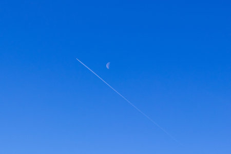 The trail of the plane and the moon on a blue background