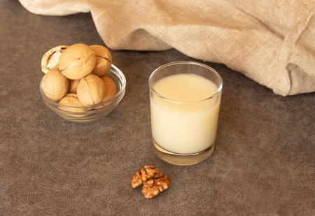 Glass cup with walnut milk and walnuts in the shell. Lactose-free milk, vegetarianism.