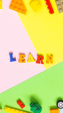 The word "LEARN" is made of colored wooden letters on a multicolored background. On the sides of the children's constructor. Vertical photo.の写真素材
