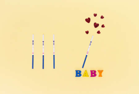 Negative and positive pregnancy test strips, red hearts and the inscription "baby". The concept of conception, waiting for the birth of a child, a family.の写真素材