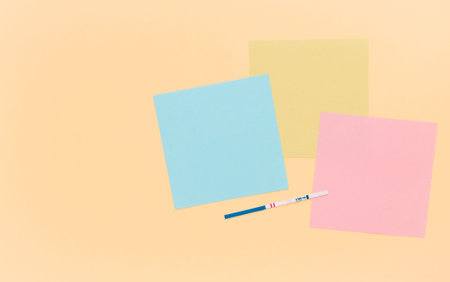 Positive pregnancy test strips, blank colored paper for notes, beige background. Template, copyspace