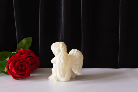 A candle in the form of an angel with wings and a red rose. The funeral symbol, the concept of...