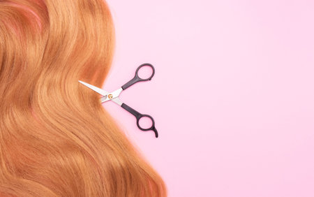 Brown artificial hair on a pink background and scissors. The concept of a hair salon, hair cutting. Copyspaceの写真素材