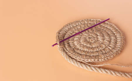 Spiral round jute napkin and crochet hook on beige background. Hobbies, needlework.の写真素材
