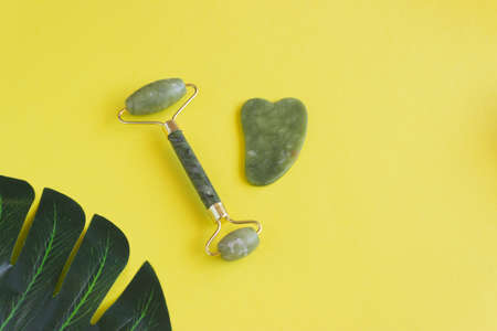 A gua sha roller and a jade stone scraper on a yellow background. Chinese massage techniqueの写真素材