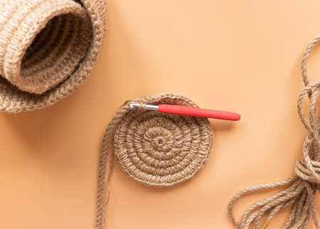 Spiral jute rope napkin and crochet hook on beige background. Hobbies, needlework.