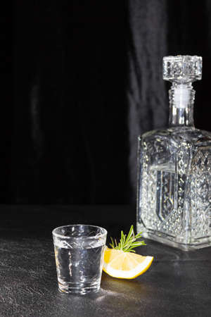 A decanter and a small glass of vodka or other colorless alcoholic beverage on a black background. A slice of lemon.の写真素材