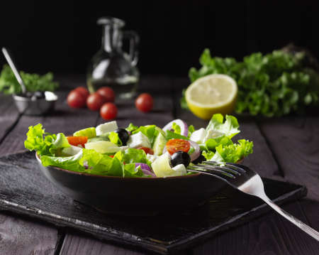 Greek salad in a plate on a cutting board on a dark wooden background. Healthy vegetarian food. Feta cheese, lettuce leaves, cherry tomatoes.の写真素材