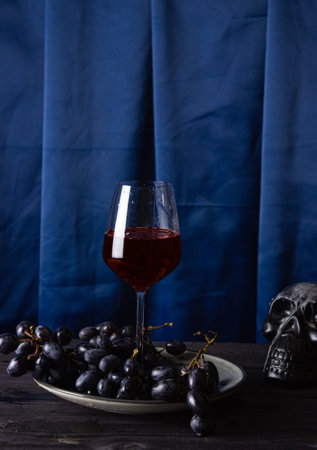 Red wine in a glass glass, grapes on a plate and part of a skull on a blue fabric background. The concept of magic, mysticism and esotericism.の写真素材