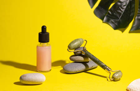 Cosmetic product in a glass bottle with a pipette and gua sha scraper and roller. Smooth stones nearby. The concept of skin care, cosmetology.の写真素材