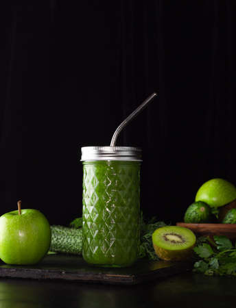 Green smoothie in a glass glass on a black background. Kiwi, apples, cucumbers and greens. Cooking healthy food. Zero weist, a metal tube.の写真素材