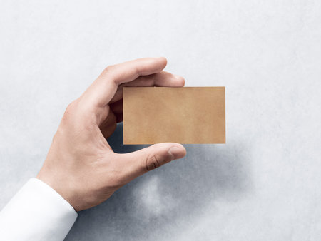Hand hold blank plain kraft business card design mockup. Clear calling card mock up template holding arm. Visit pasteboard craft paper display front. Small offset texture card print. Business identityの写真素材