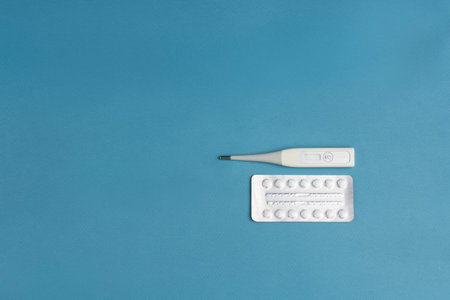 Electronic thermometer with a flexible tip and a blister of square tablets on a blue background