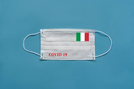 Medical mask with the flag of Italy and the inscription COVID-19 on a blue backgroundの写真素材