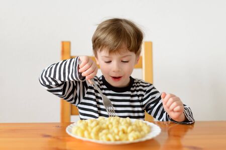 A boy sits at a table and eats a pasta dishの写真素材