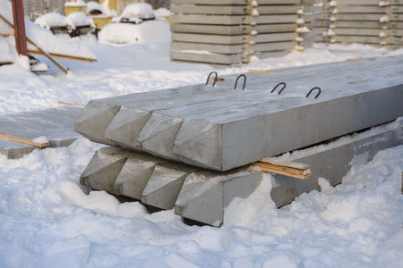 Reinforced concrete piles are stored in the warehouse of the precast concrete plant in winter conditions. The product warehouse is covered with snowの写真素材