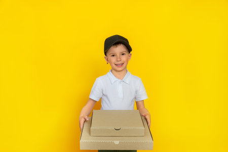 A baby pizza delivery guy holds boxes in there and smiles happily, looking straight into the camera. Dressed in a black cap and white T-shirtの写真素材