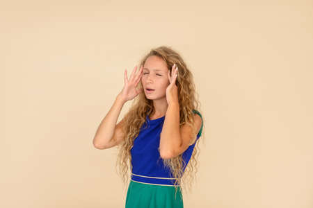Girl with long curly hair touches her temples with her hands, demonstrating a severe headache, beige isolated backgroundの写真素材