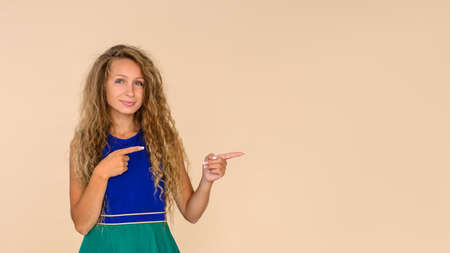 Young woman on a beige isolated background points with her fingers to a free space for an inscription, insert into an advertisementの写真素材