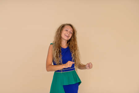 Girl with long blond curly hair smiles and dances on a beige background in the studio, half-length portraitの写真素材