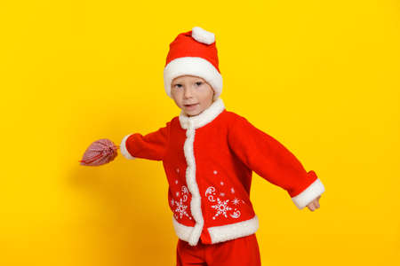 Handsome caucasian little boy waving a sack of gifts on a yellow background dressed as Santa Clausの写真素材