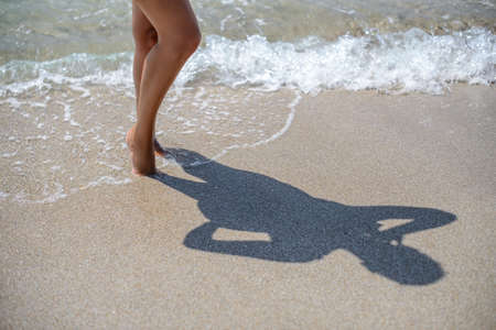 Beautiful legs of a beautiful girl standing in the water, the shadow of a girl on the sandの写真素材
