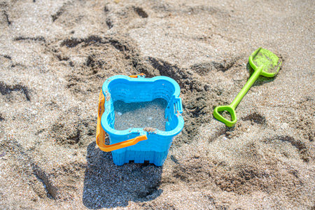The concept of children's holiday at the sea. Children's toys on the sand: blue bucket, green...