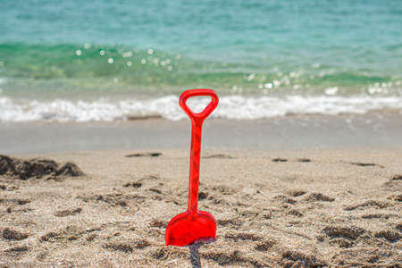 The concept of children's relaxation on the beach. A red child's spatula is stuck in the sand against the background of the wash. No peopleの写真素材