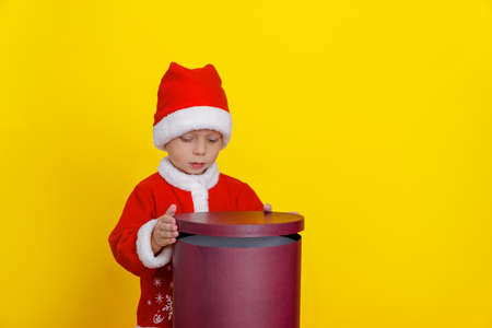 Caucasian Child in Santa Claus Clothes Opens Red Round Gift Boxの写真素材