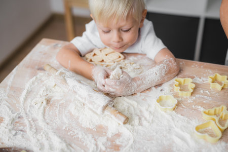 Little boy prepares homemade cookies, sprinkles flour all over the table and kneads the dough with his handsの写真素材