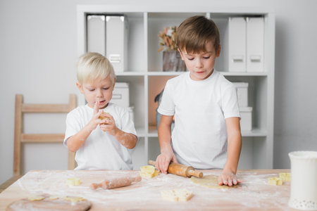 Home cooking concept: two boys prepare cookies, one rolls out damp dough, the second sculptsの写真素材