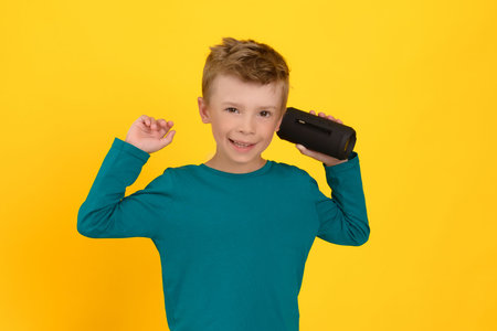 A cute child holds a portable musical device in his hands and smiles, he likes to listen to music,...