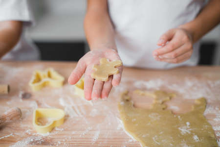 Close-up of a child's palm with a piece of raw dough biscuits resembling a bear, in the background a kitchen table soaked in flourの写真素材