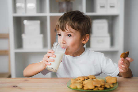 Caucasian boy child sits at the table, drinks milk and eats cookiesの写真素材