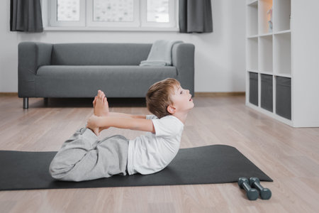 Boy child practicing yoga, stretching in dhanurasana exercise, bow pose, working out wearing sportswear, t-shirt, pantsの写真素材
