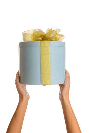 Female hands are holding blue round gift box with yellow bow on white isolated backgroundの写真素材