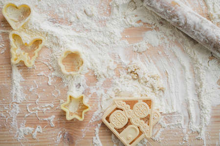 Top view, kitchen table with flour sprinkled, plastic culinary molds, wooden rolling pin and pieces of dough laid outの写真素材