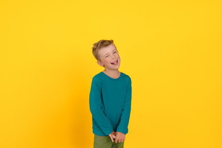 Little boy stands on a yellow background smiles and shows tongueの写真素材