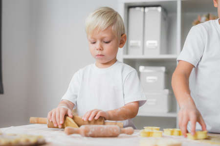 Little boy prepares cookies. He rolls raw dough with a rolling pin with a serious look.の写真素材
