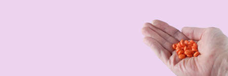hand of an elderly man holding a handful of red pills, pale pink background, banner concept, place for textの写真素材