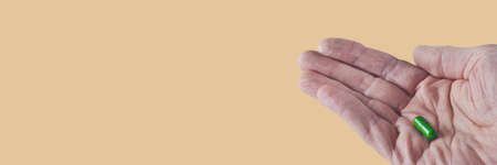 one green capsule with drug lie on a man's wrinkled palm, isolated image on background, banner conceptの写真素材